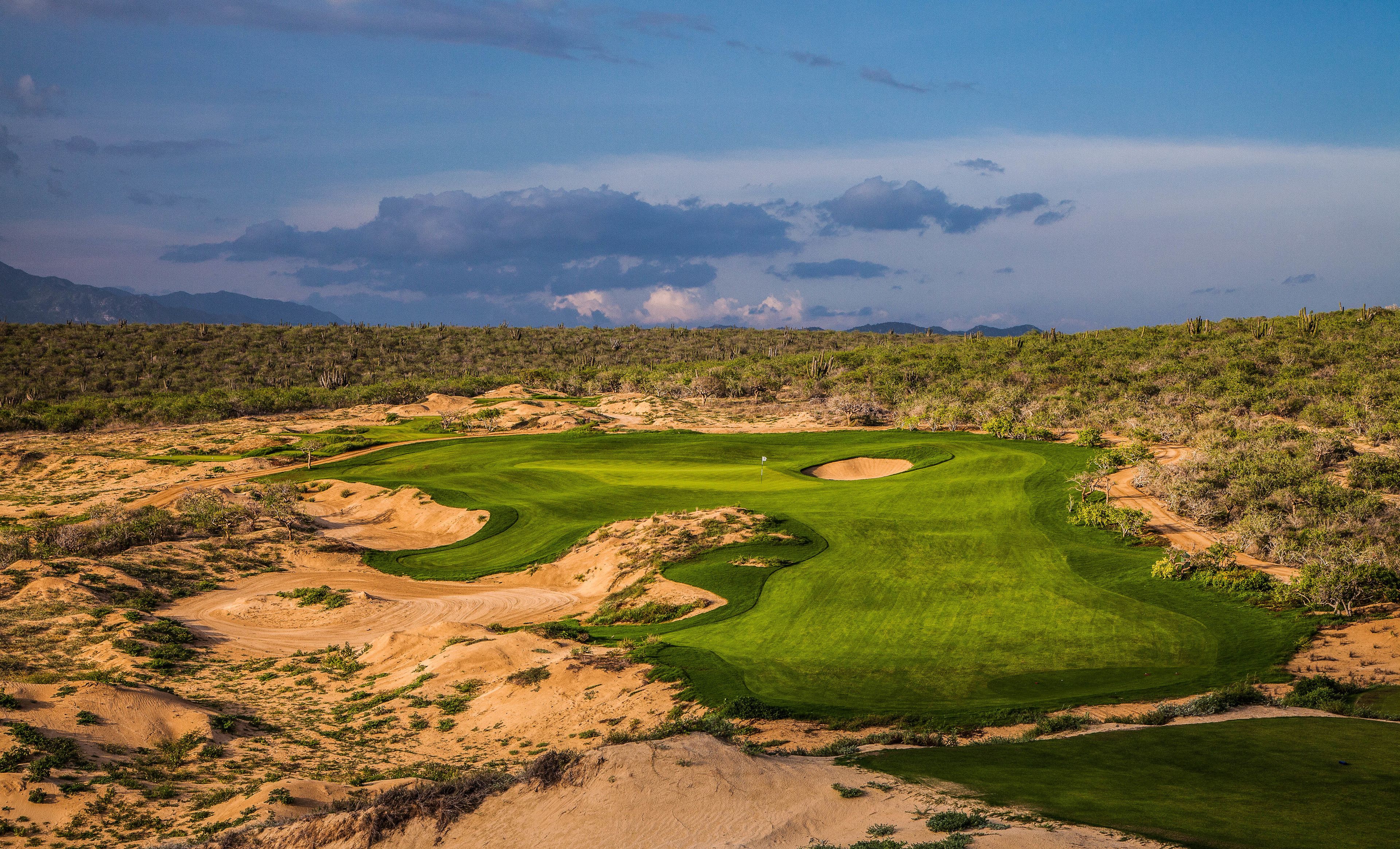 A golf course with sand bunkers, a flag, and a clear sky.