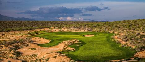 A golf course with sand bunkers, a flag, and a clear sky.
