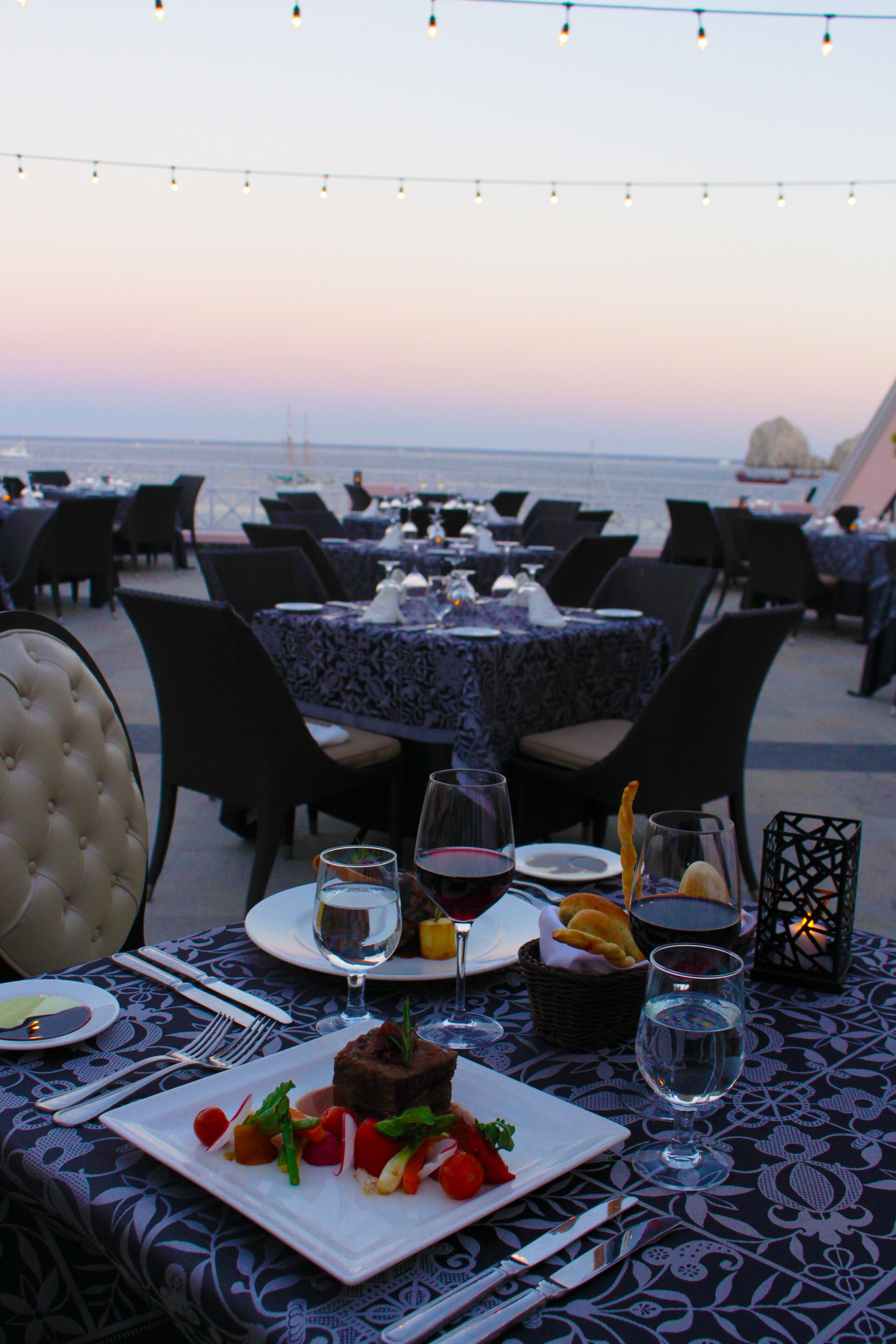 An outdoor dining area with tables set for a meal, overlooking the sea.