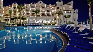 Zona de piscina de hotel con sillones de descanso y palmeras.