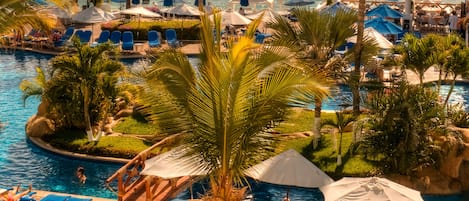 A resort pool area with lounge chairs, umbrellas, and palm trees.