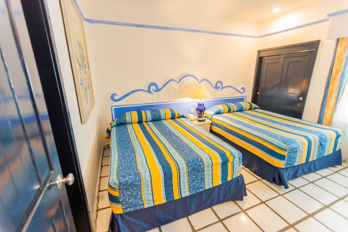 A room with two beds, a nightstand, a lamp, and a door.