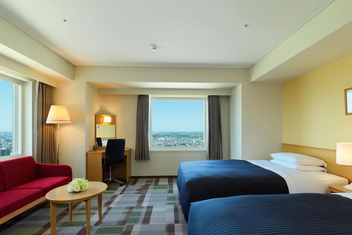 A hotel room with two beds, a desk, a chair, a small table, and a red sofa.