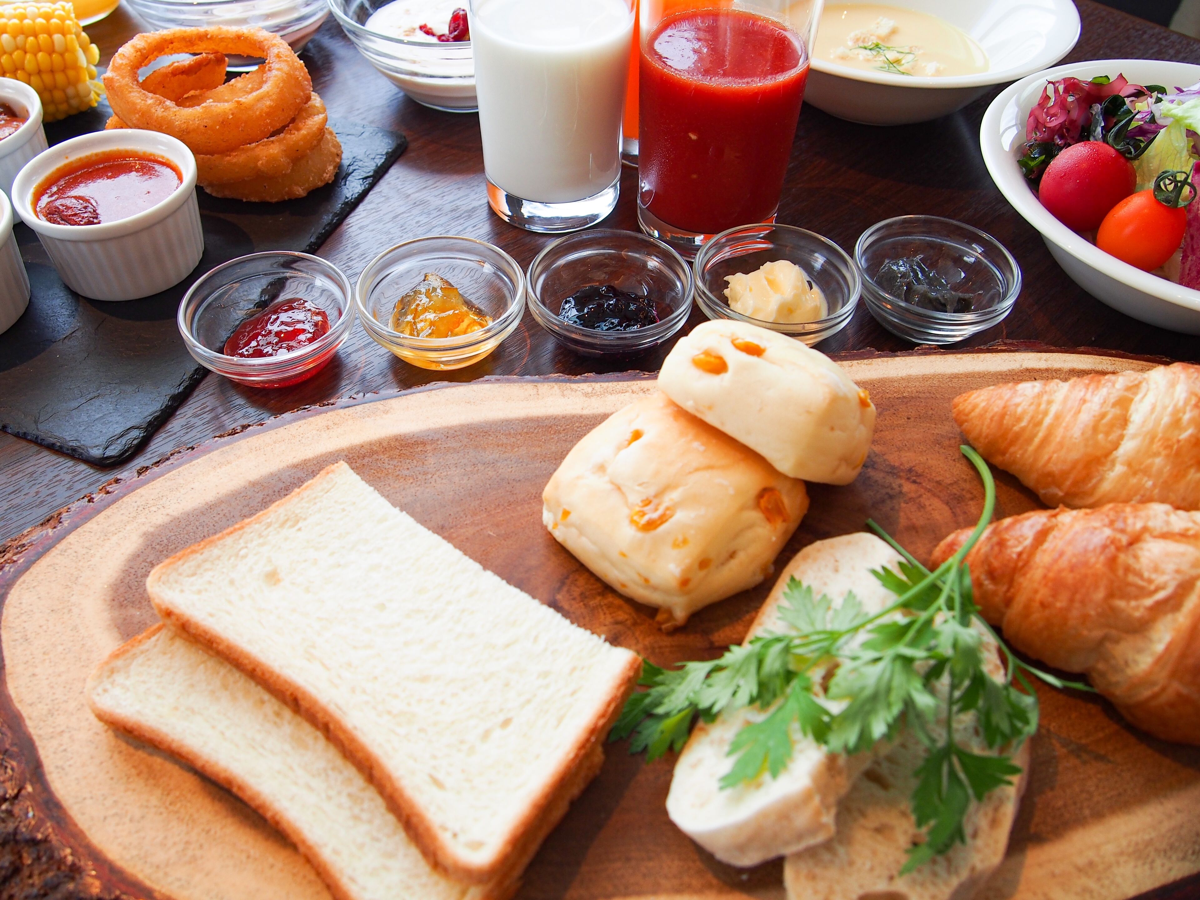 Une table en bois sur laquelle sont disposés divers aliments, notamment du pain, des croissants et des condiments.