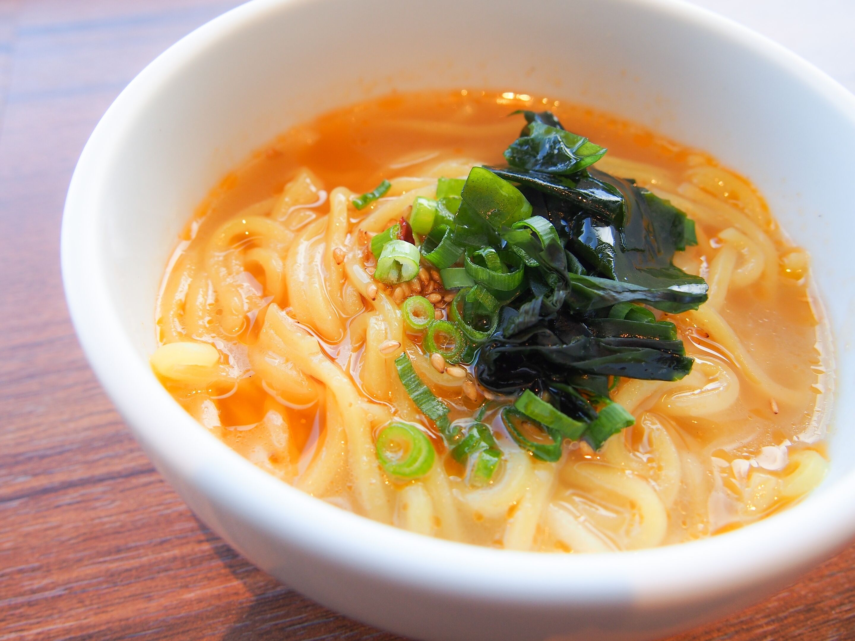 A bowl of ramen with noodles, broth, green onions, and seaweed.