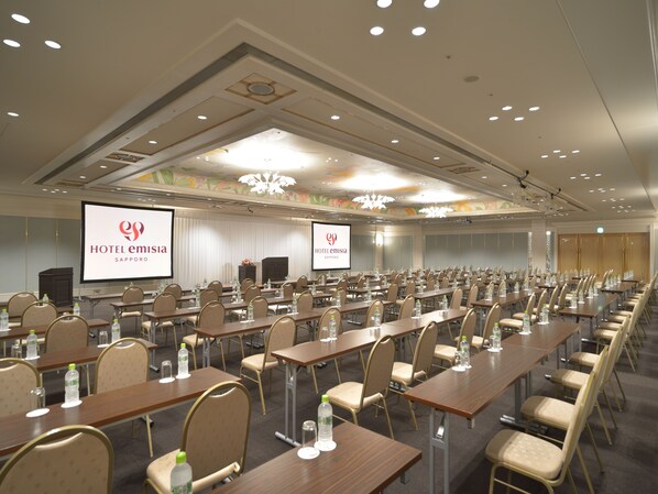 A hotel conference room with multiple tables, chairs, and a large screen displaying the hotel's logo.