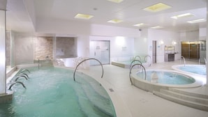 En stor inomhuspool med flera banor, ett separat område med bubbelbad och en receptionsdisk i bakgrunden.