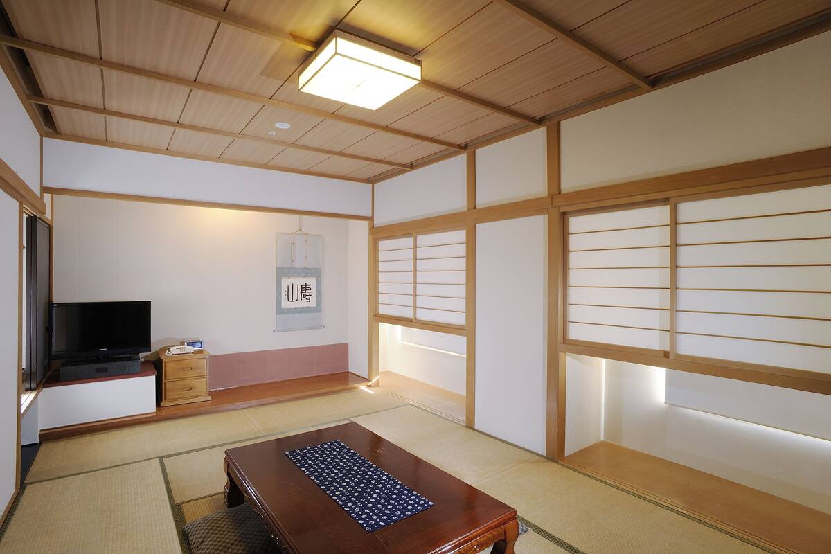 A traditional Japanese room with tatami flooring, a low wooden table, a television, and sliding doors.