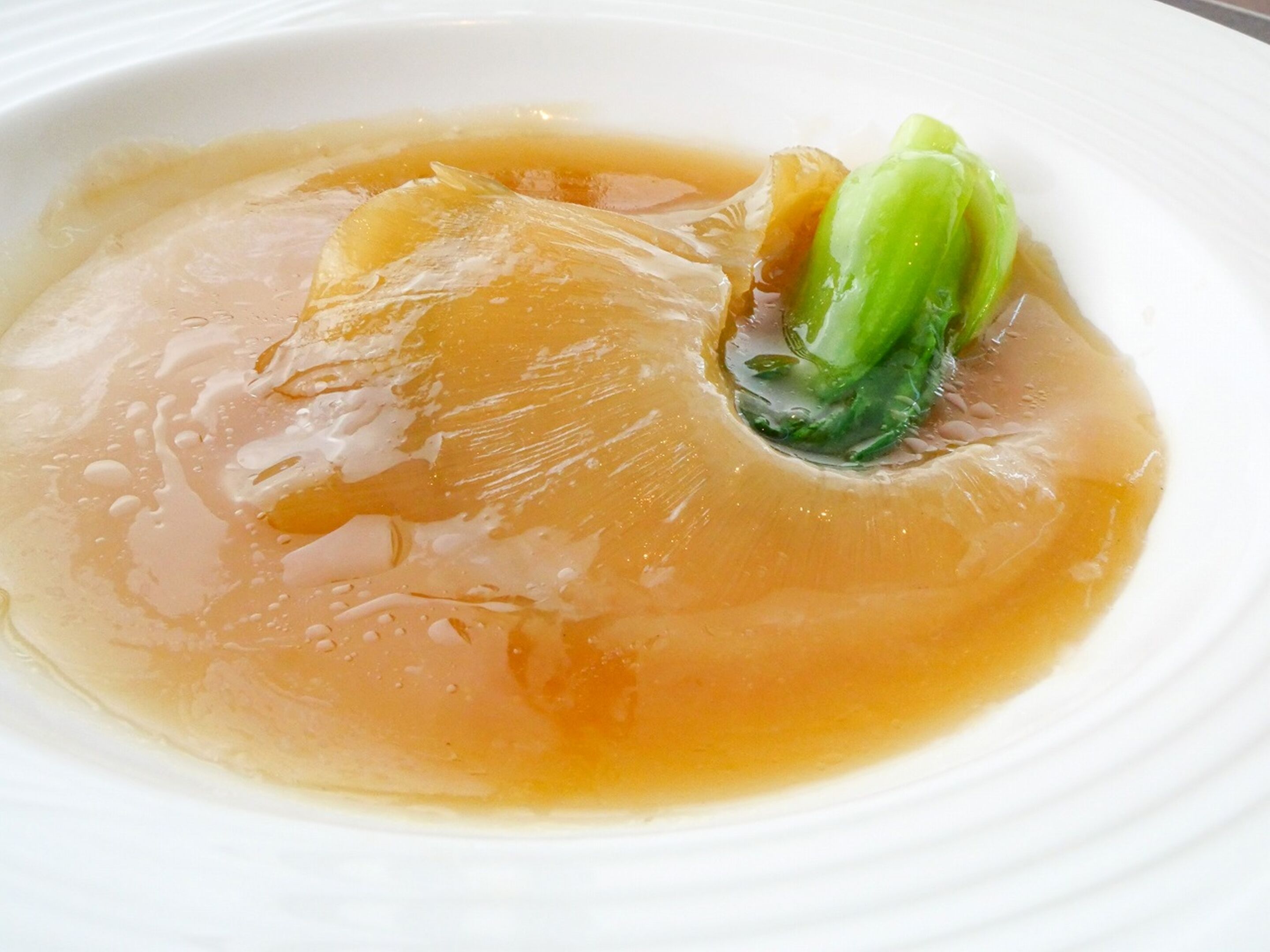 A bowl of soup with a clear broth and a piece of green vegetable.
