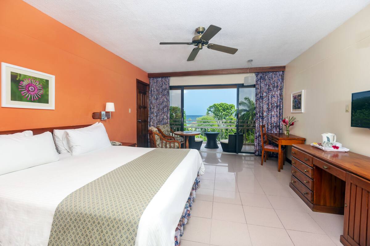 A hotel room with a bed, a desk, a chair, a table, and a balcony with a view.