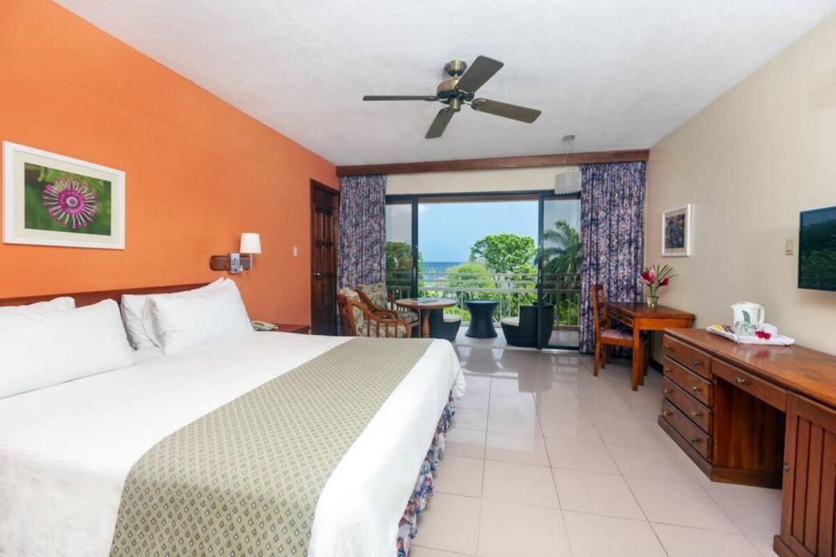 A hotel room with a bed, a desk, a chair, a table, and a balcony with a view.