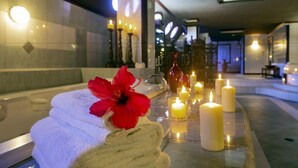 A spa area with a stack of white towels, a red hibiscus flower, and several lit candles on a reflective surface. - Le Grand Courlan Spa Resort - Adults Only (Black Rock)
