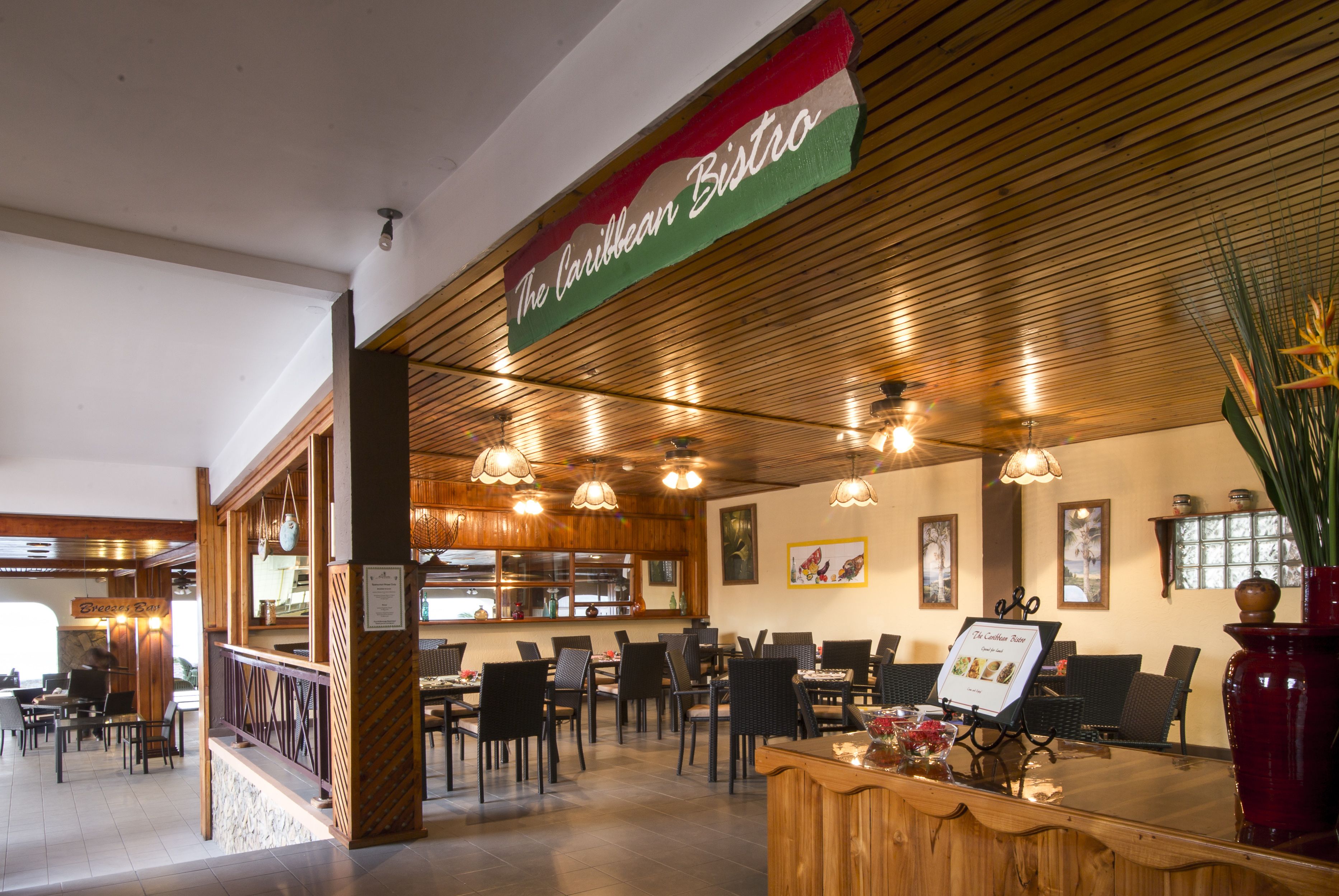 A restaurant interior with wooden ceiling, multiple tables, chairs, and hanging pendant lights.