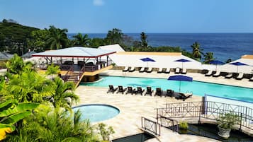 A resort pool area with lounge chairs, umbrellas, and a view of the ocean.