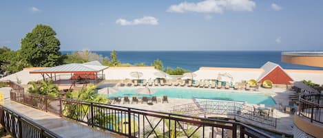 A pool area with lounge chairs and umbrellas, a wooden deck, and a view of the ocean.