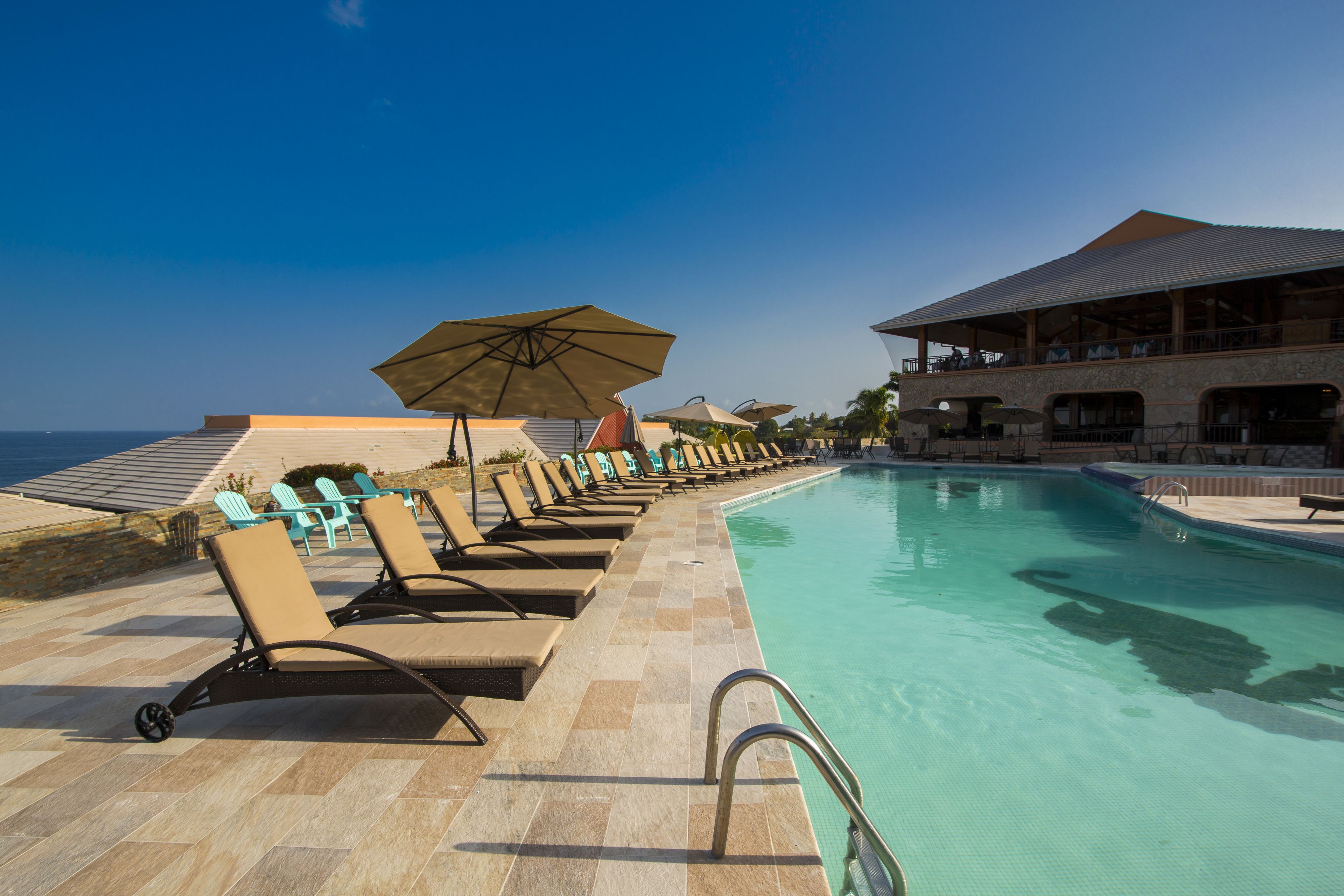 A poolside area with lounge chairs and umbrellas, a clear sky, and a view of the ocean.