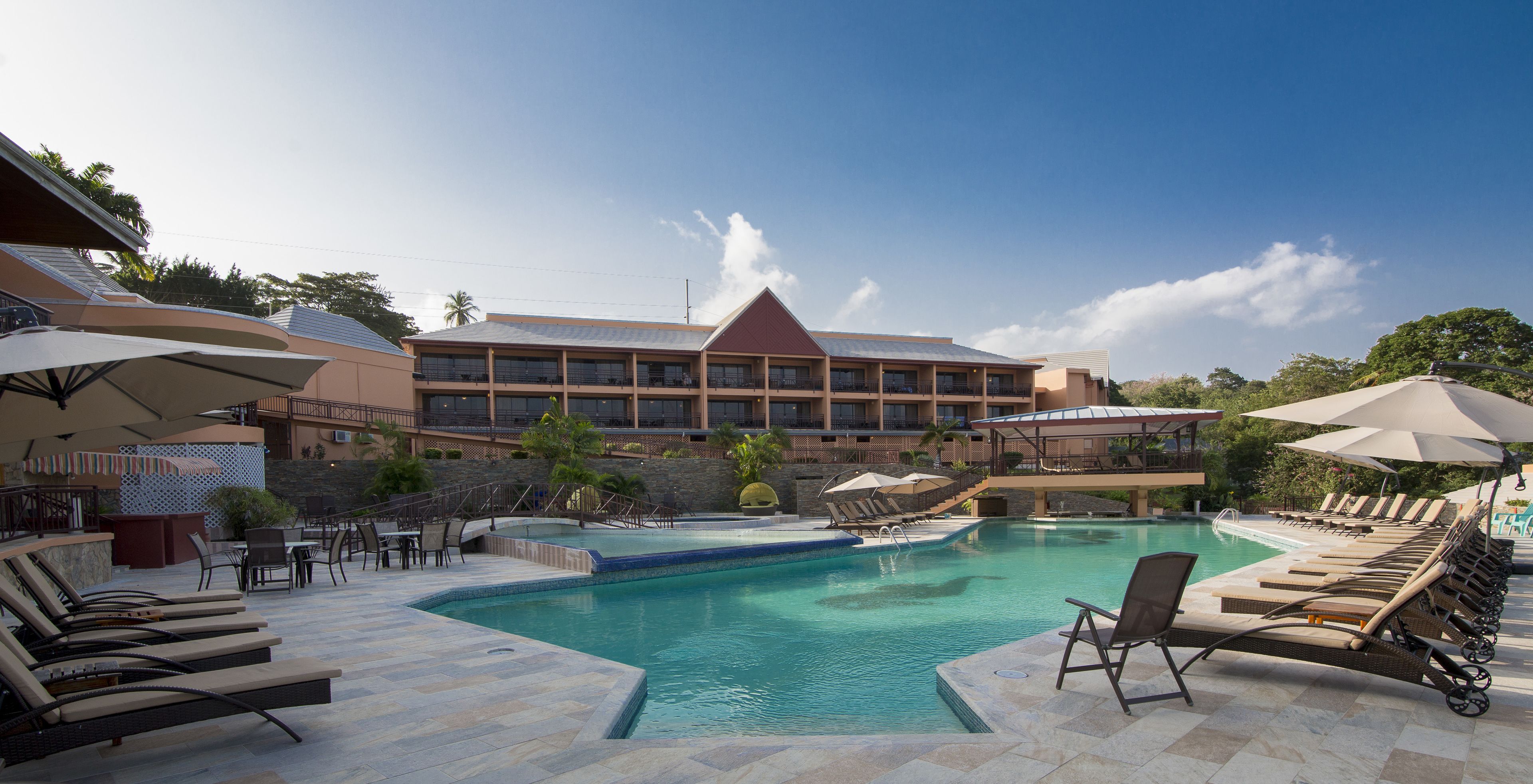 A resort pool area with sun loungers, umbrellas, and a large building in the background.