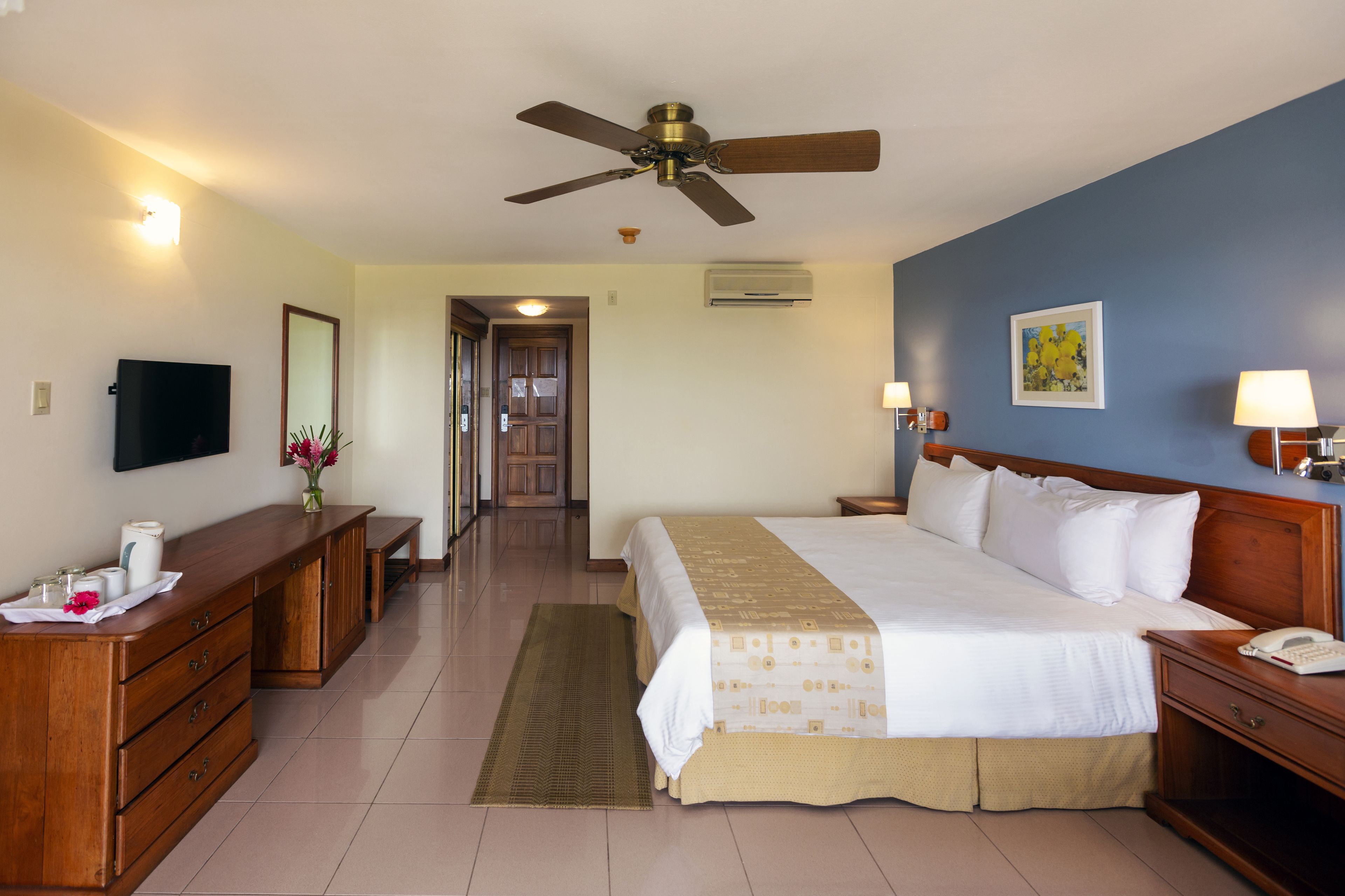 Una habitación de hotel con una cama grande, un escritorio, un televisor y un ventilador de techo.