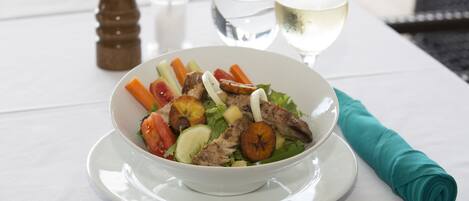 A white table with a bowl of salad, two glasses of white wine, and a rolled green napkin.