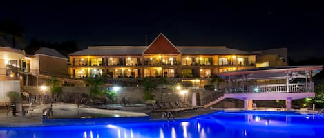 A hotel with a swimming pool, outdoor seating, and a well-lit building facade.