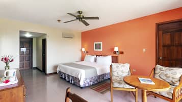 A hotel room with a bed, a wooden table, two chairs, a ceiling fan, and a door.