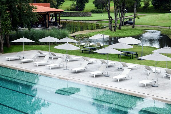 A swimming pool with lounge chairs and umbrellas, a small waterfall, and a golf course in the background. - Hotel Avandaro Golf And Spa (Valle de Bravo)