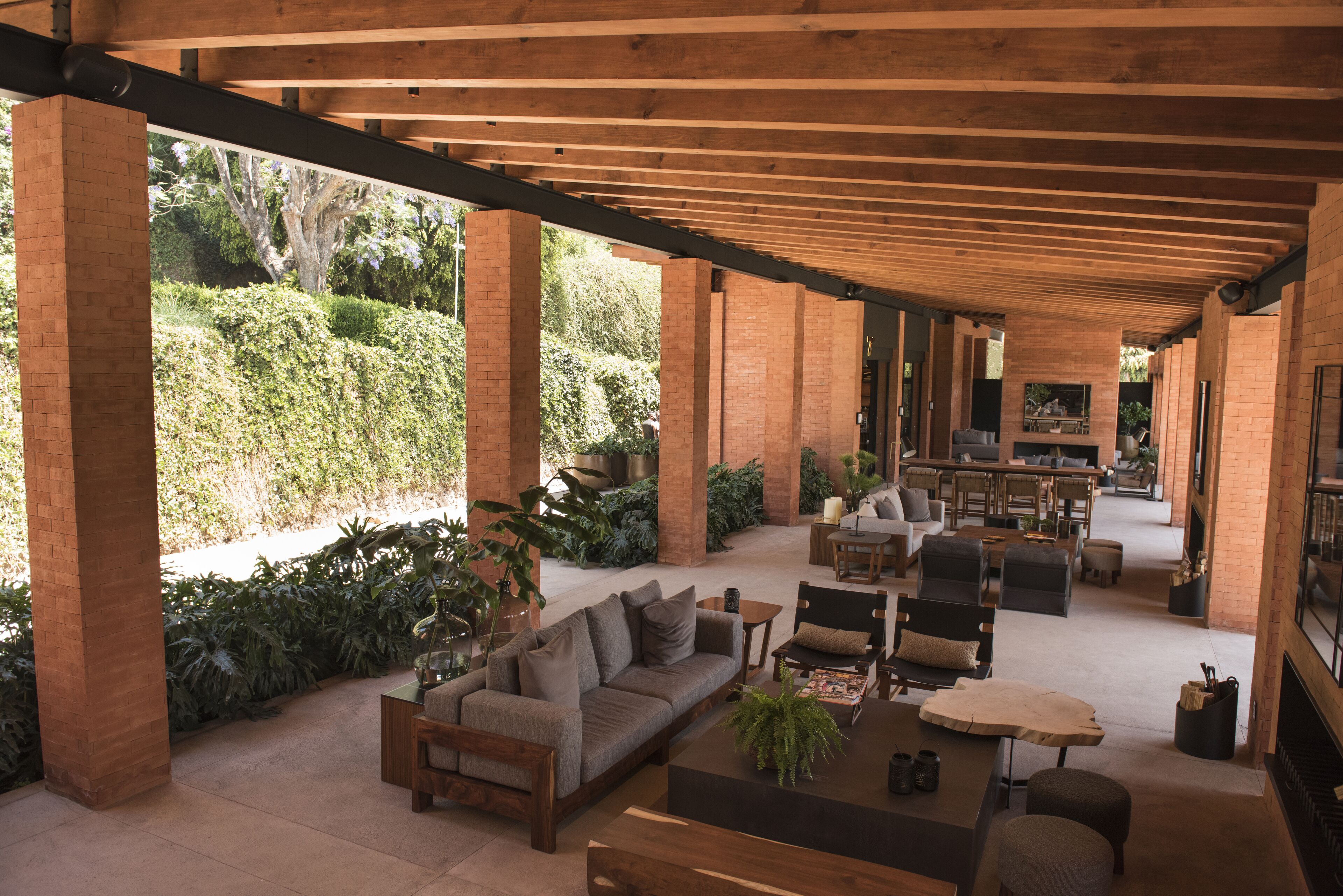 An open-plan living area with a wooden ceiling, brick pillars, and a variety of seating arrangements including sofas and chairs.