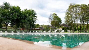 Piscina con sillas de descanso y sombrillas, rodeada de árboles y vegetación.