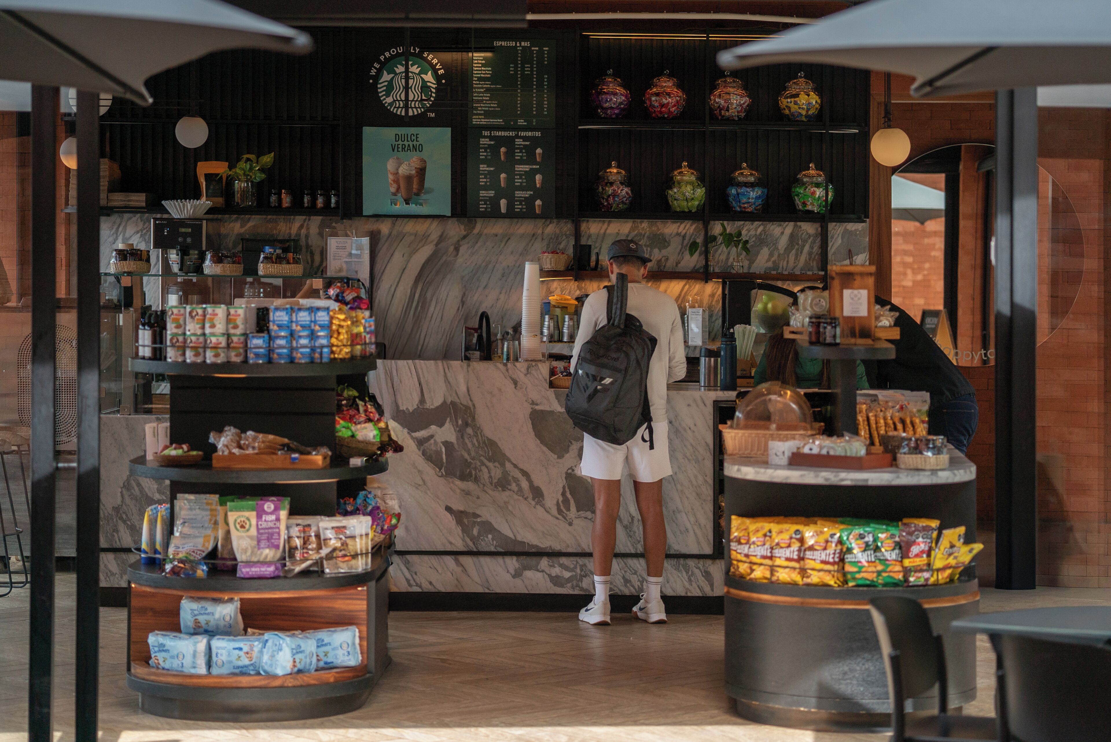 A coffee shop interior with a marble counter, shelves with jars, and a menu board.