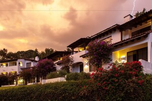 Un edificio de varios pisos con balcones y un jardín con plantas en flor.