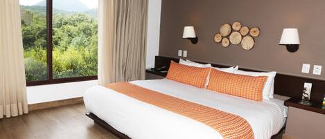 A bedroom with a large bed, two bedside lamps, a nightstand, a view of a forest through a window, and a red rug.