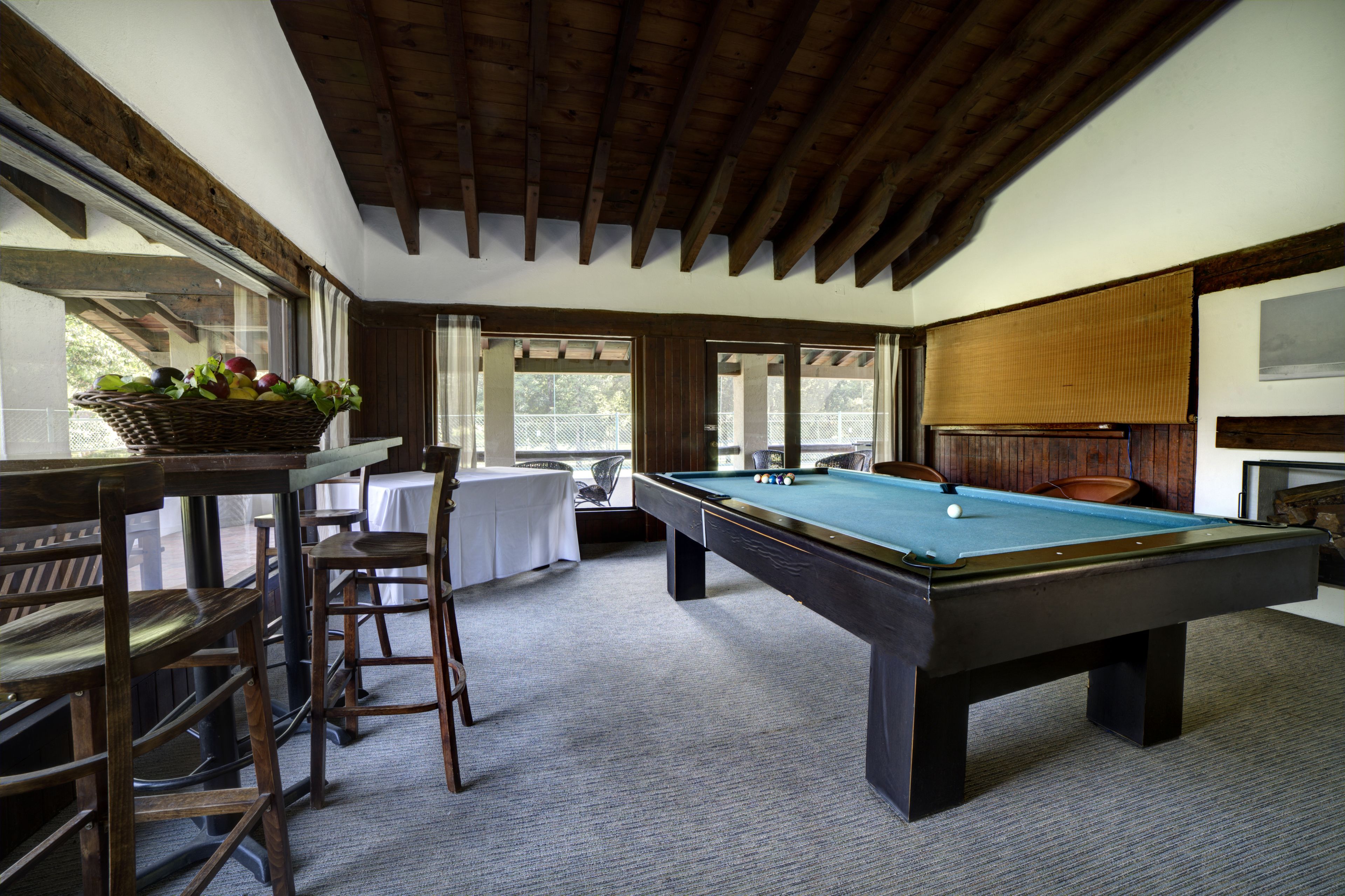 A pool table with a green felt surface, wooden chairs, a wicker basket with fruits, and a white tablecloth.