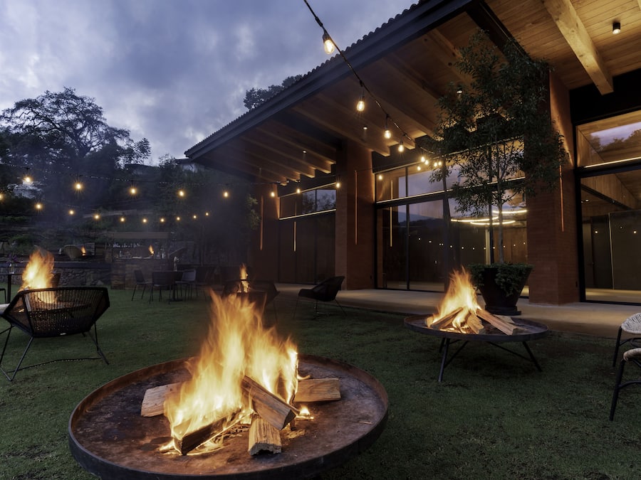 A modern outdoor patio with a fire pit, seating, and string lights.