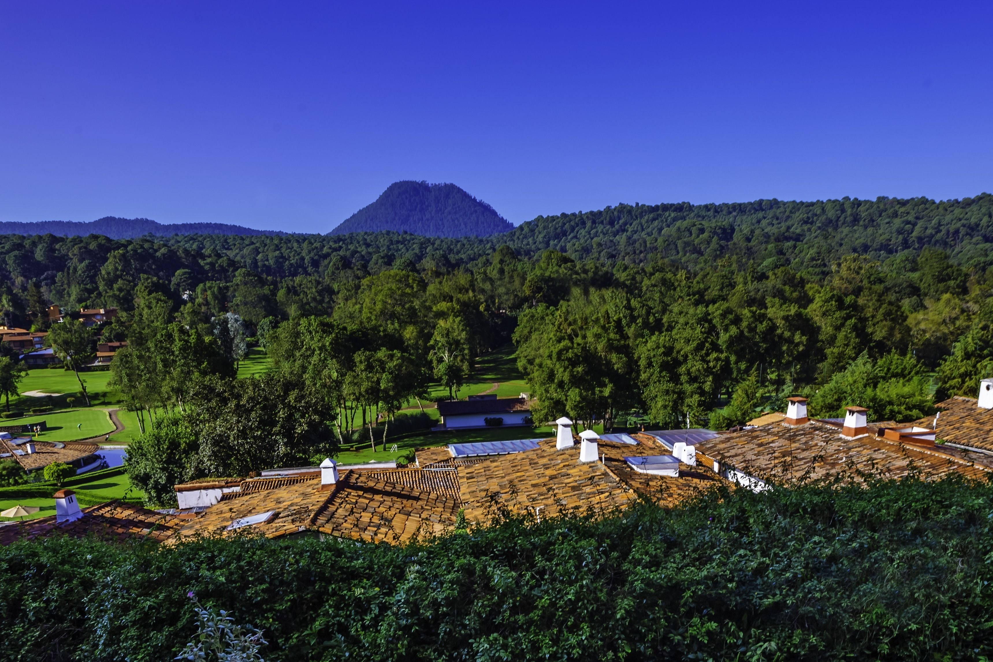 Paisaje rural con una montaña al fondo, un campo de golf y varios edificios con paneles solares.