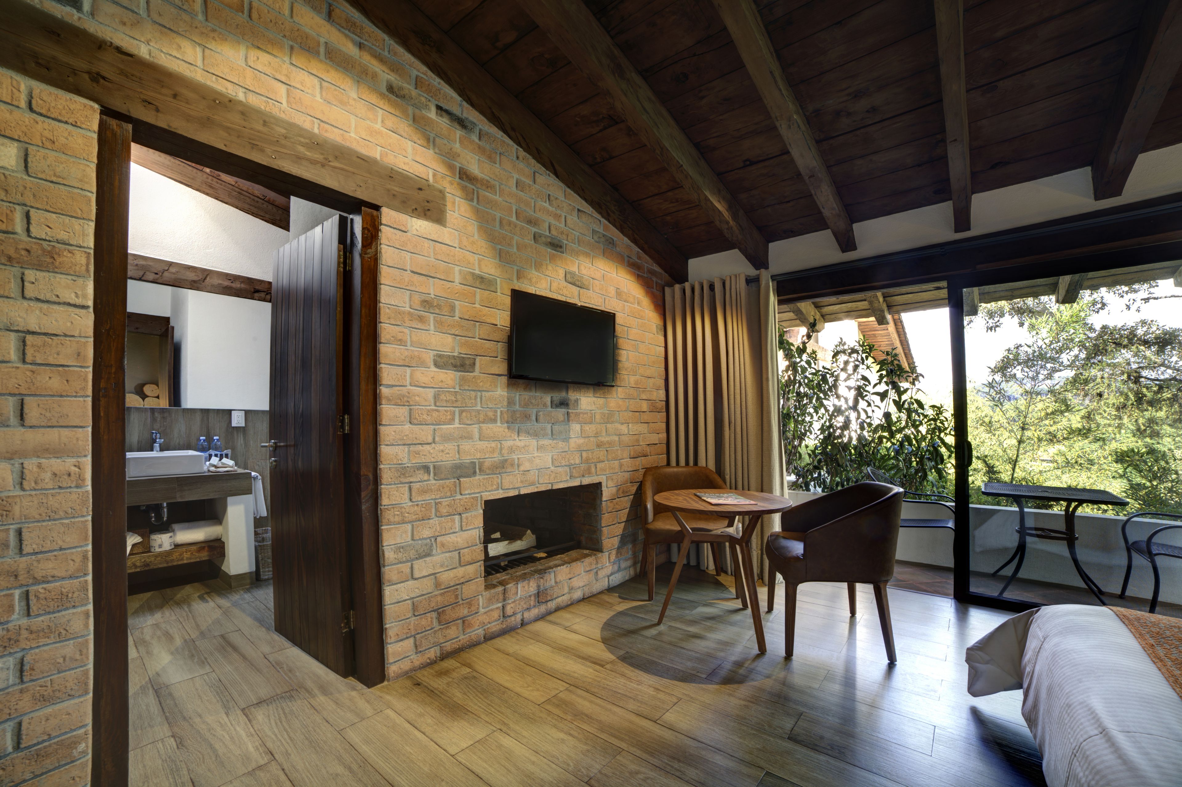 Una habitación con pared de ladrillo, techo de madera, chimenea, televisor, mesa de comedor con sillas y cama.
