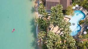 Vue aérienne d’un complexe hôtelier avec une plage, une piscine et des palmiers.
