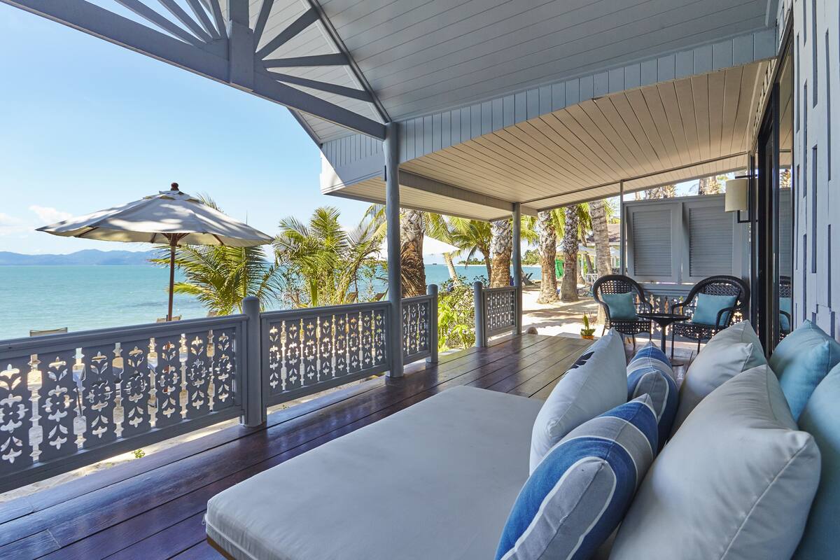 Ein überdachter Außenbereich mit Meerblick, einer Holzterrasse und einem weißen Sofa mit blauen Kissen.