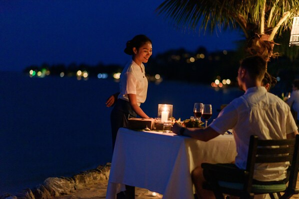 A table set for two at a beachfront restaurant with a candle and wine glasses. - Paradise Beach Resort Samui (Koh Samui)