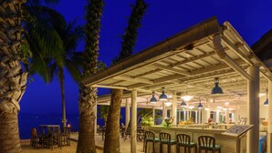 Un espace bar extérieur doté d’un coin salon abrité, de palmiers et offrant une vue sur la mer.