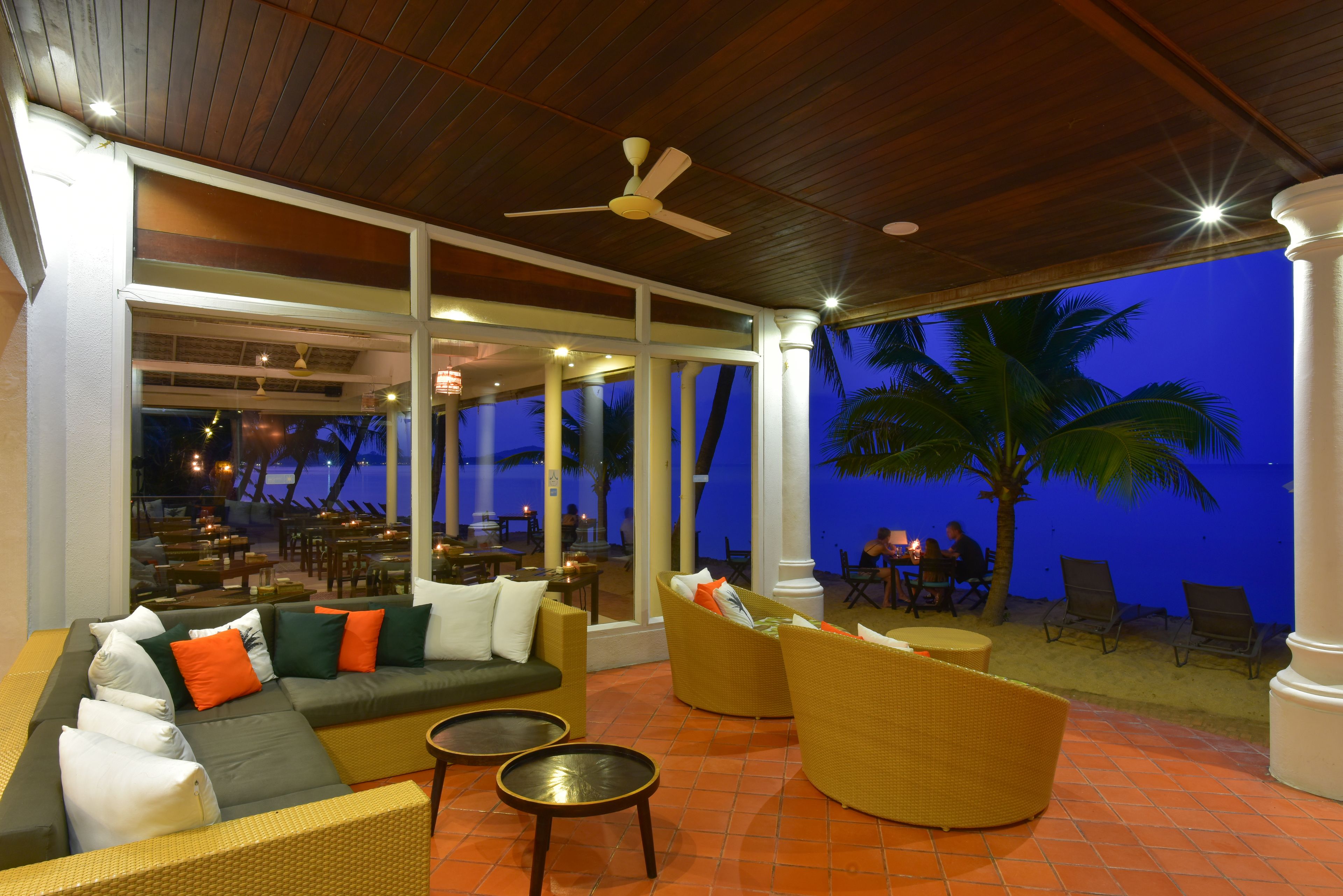 A spacious outdoor seating area with a large sofa, wicker chairs, and a ceiling fan.