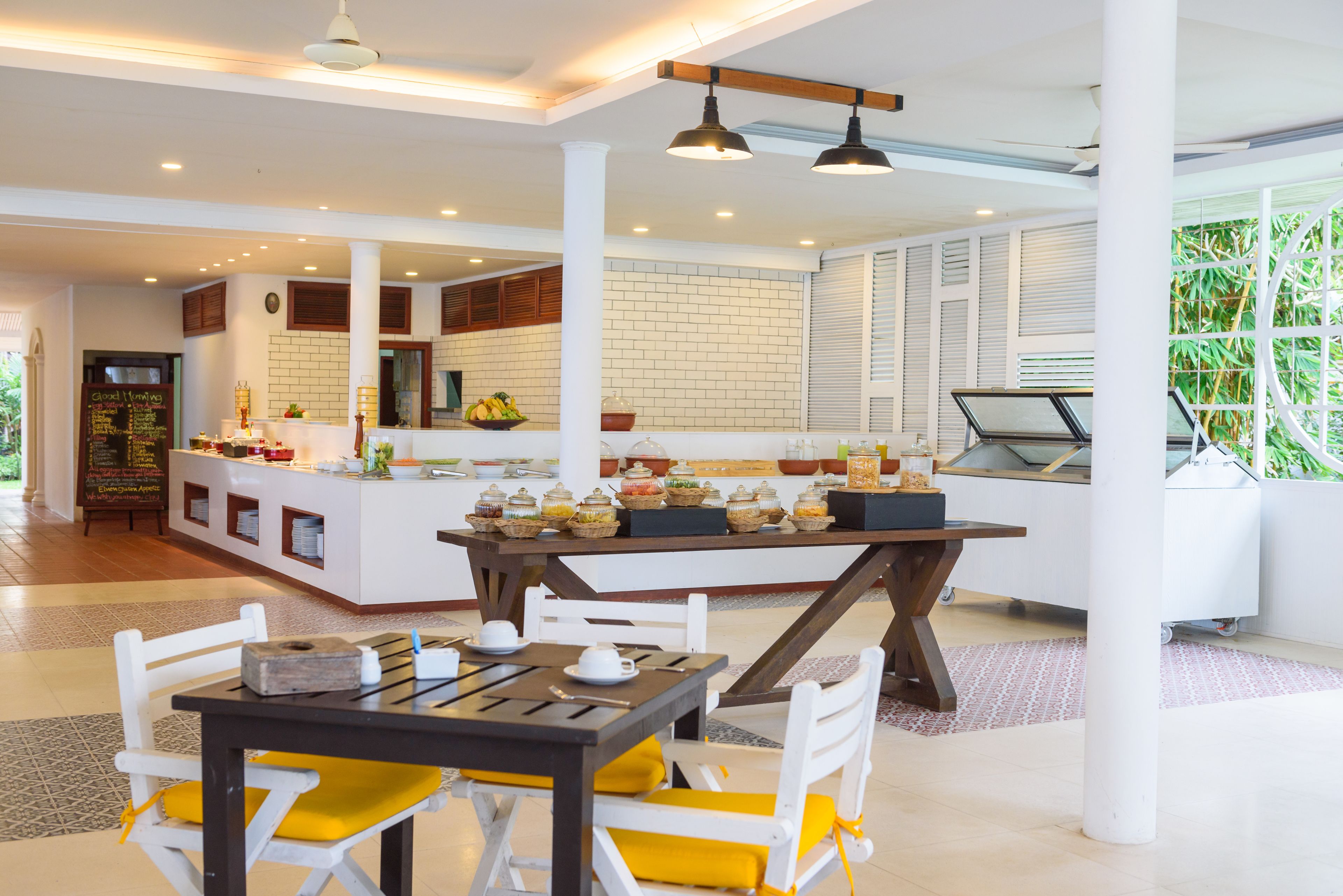A modern hotel lobby with a central island counter, white furniture, and a view of greenery outside.