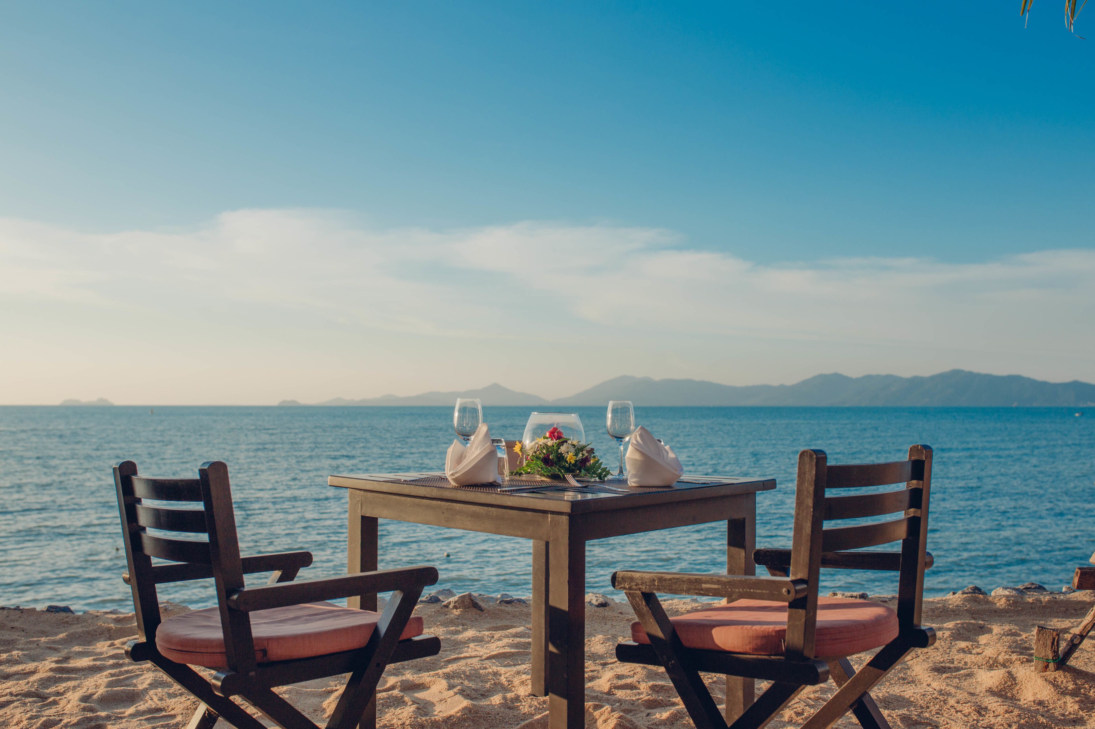 A wooden table set for two with a view of the sea and mountains in the background.