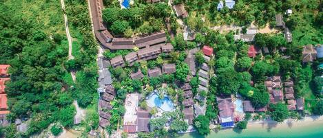 Vista aèria d'un complex turístic amb diverses piscines, una platja i vegetació tropical abundant.