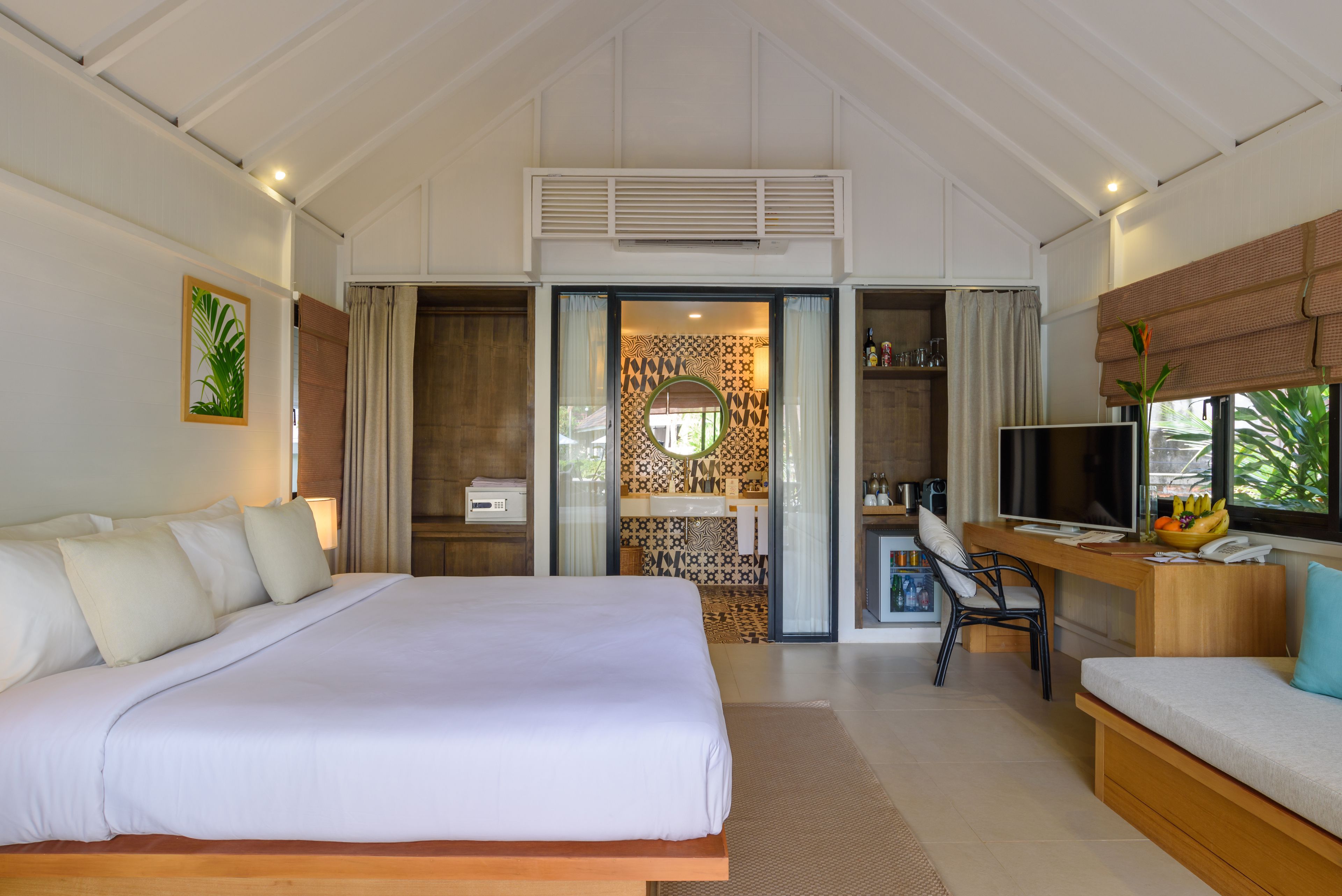 A hotel room with a large bed, a desk with a computer, a TV, and a small kitchenette.