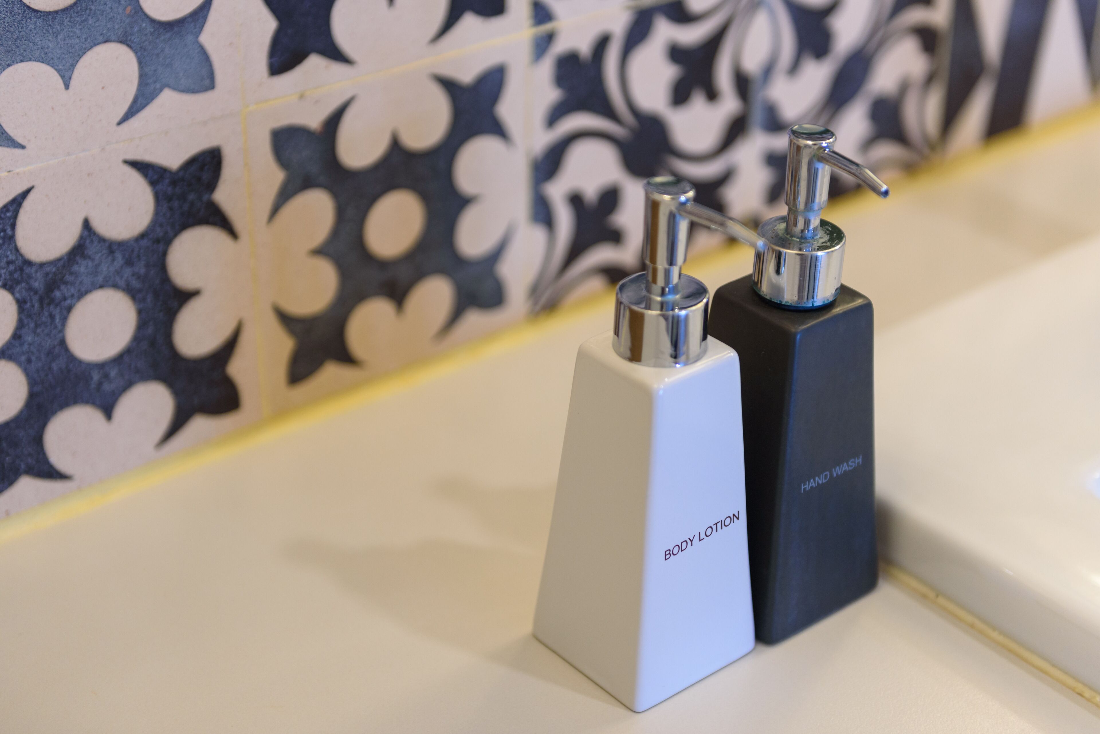Two hand soap dispensers on a bathroom counter with a patterned tile backsplash.