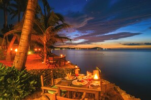 An outdoor dining area with a table set for two, overlooking a calm body of water and a sunset sky. - Paradise Beach Resort Samui (Koh Samui)