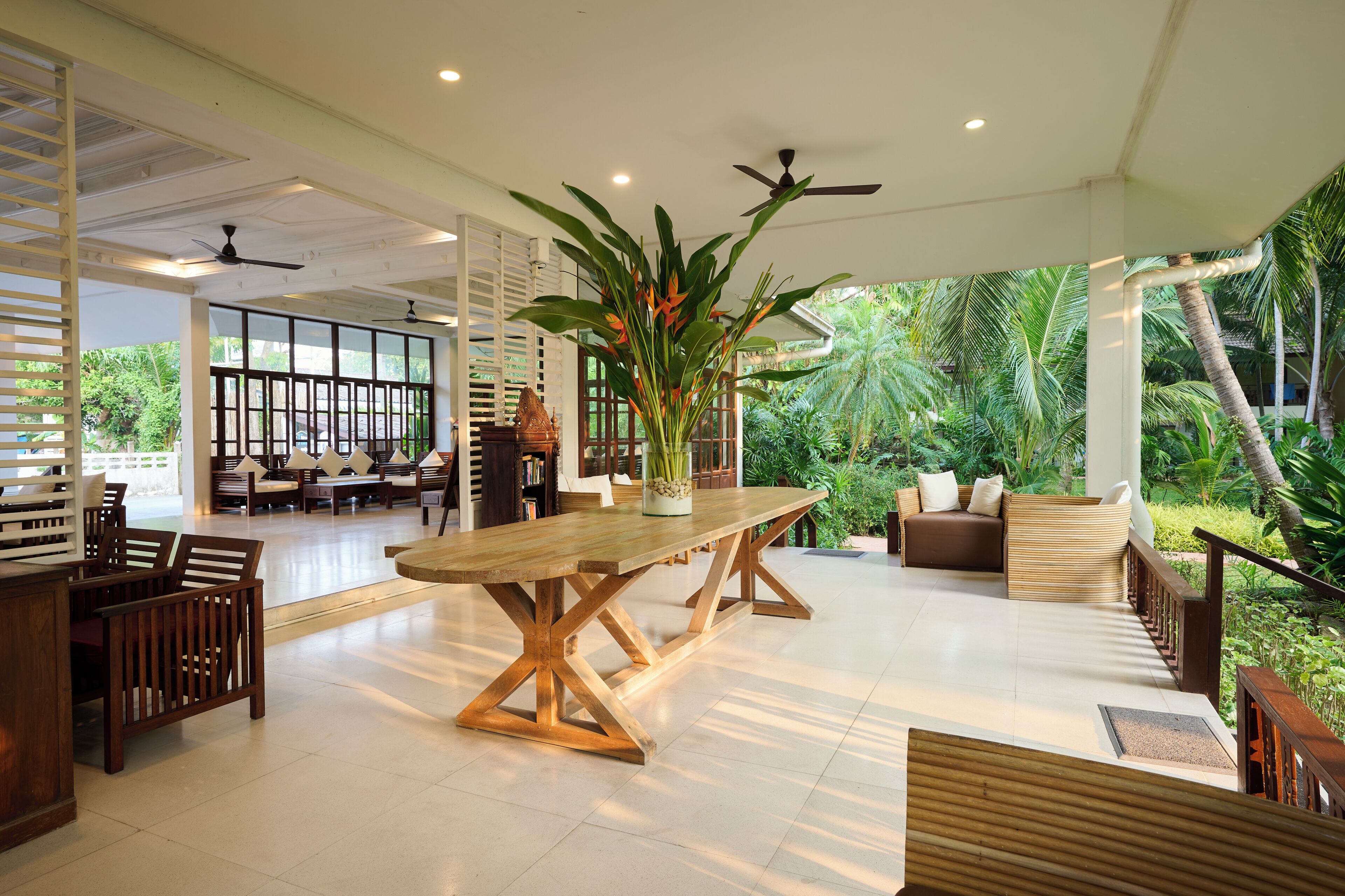 A spacious indoor area with a large wooden table, seating arrangements, and a view of lush greenery outside.
