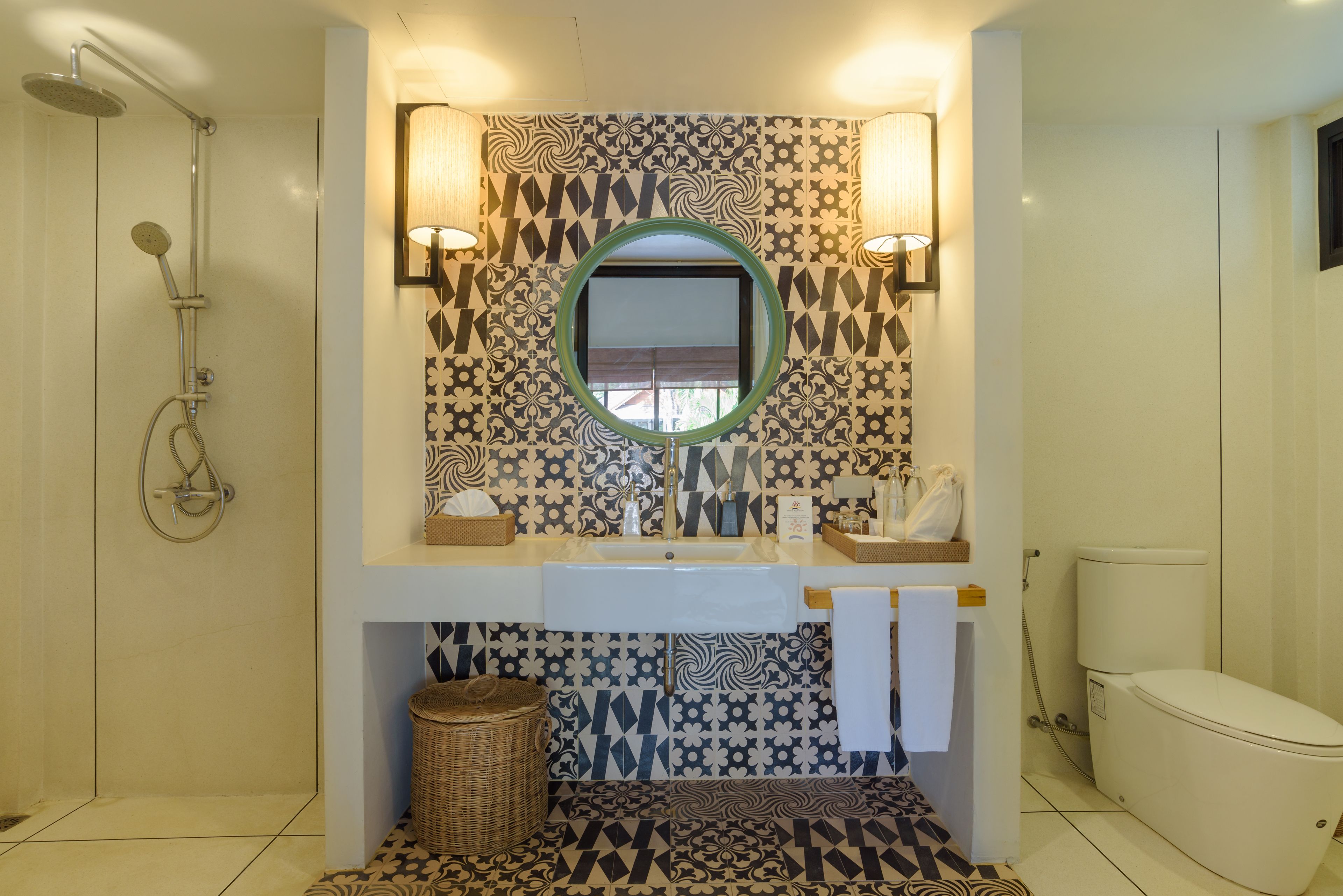 Un baño con un respuesto de azulejos estampados, un espejo redondo, un lavabo, un inodoro y una ducha.