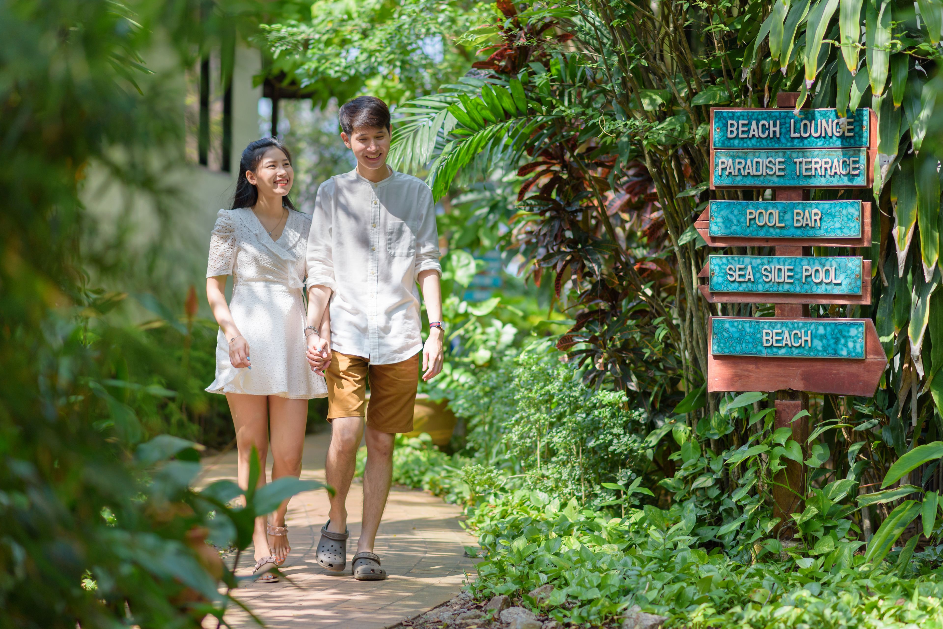 A couple walking beside a signpost with directions to various amenities including a beach lounge, paradise terrace, pool bar, and sea side pool.