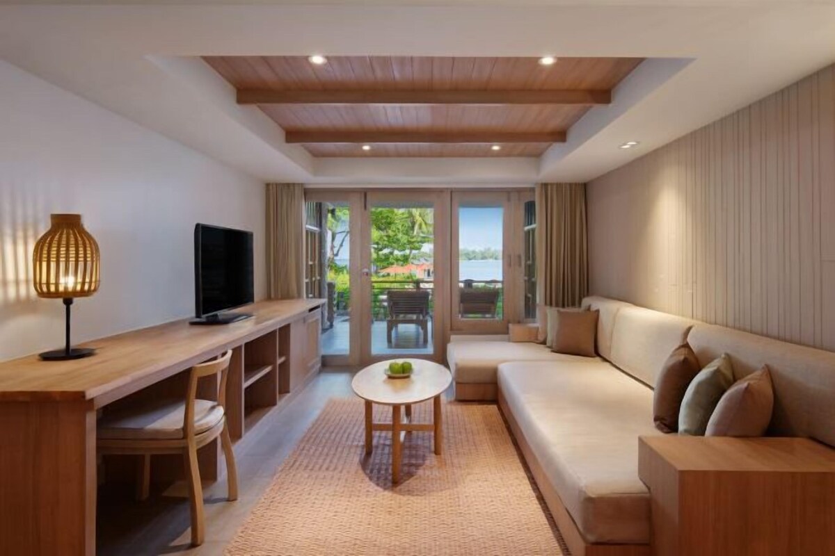 Una sala de estar moderna con un escritorio de madera, un sofá, un televisor y vistas al exterior.